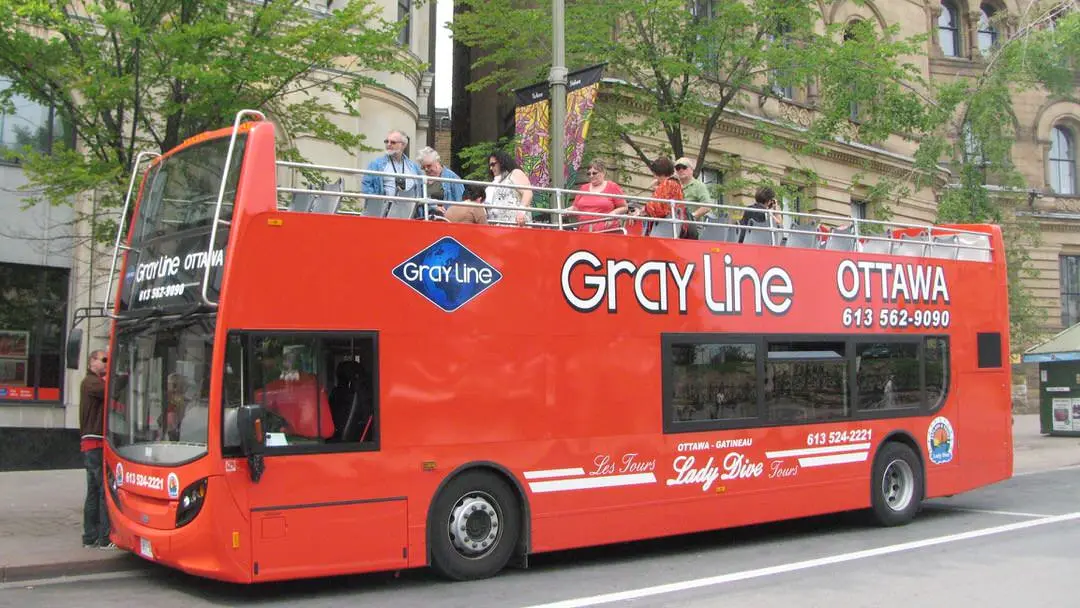 Autobus à deux étages Red Gray Line stationné sur une rue historique avec touristes à l'étage supérieur.