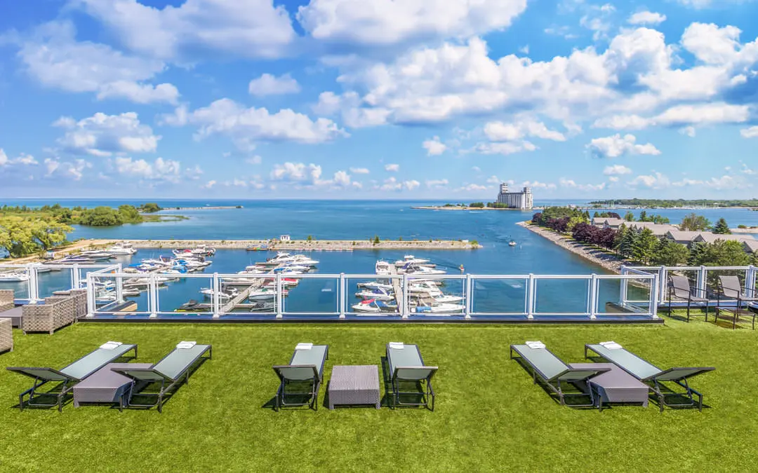 위쪽 잔디밭에 잔디 의자 3개와 탁자가 맑은 푸른 하늘 아래 정박된 보트로 가득 찬 마리나를 내려다보고 있습니다.