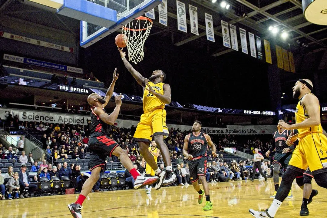 Basketballspieler in der Luft, der Ball unter Spielern mit großem Publikum in Hintergrundtribünen in den Korb wirft