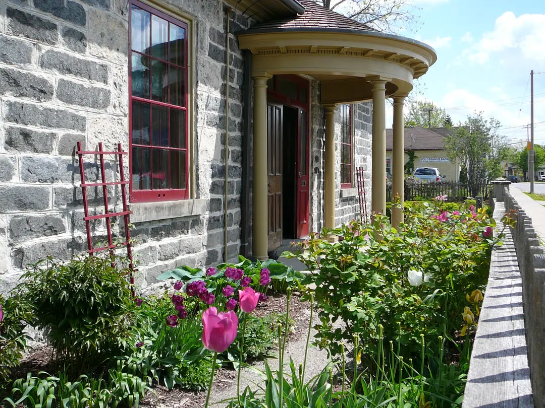 Angle view of old gray brick building with portico at front entrance and tulip garden along front wall