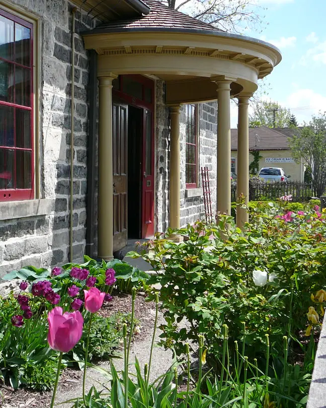 Vue en angle d'un ancien édifice de brique grise avec portique à l'entrée principale et jardin de tulipes le long de la façade.