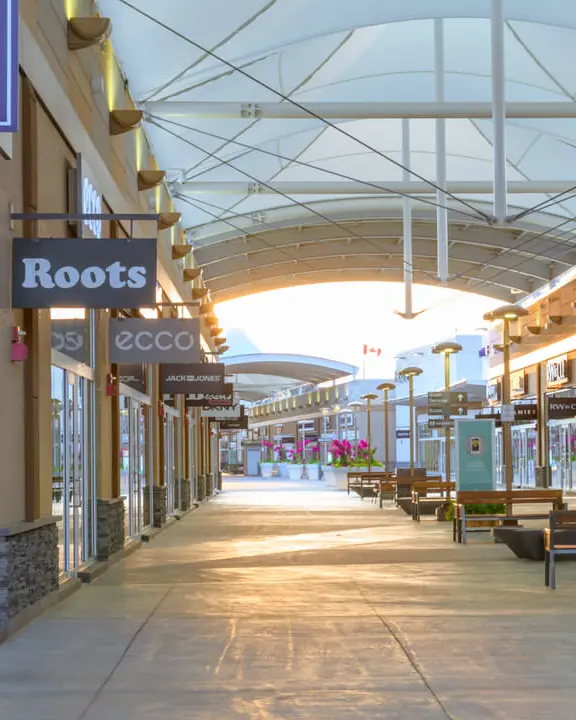 Very long indoor mall with row of benches down middle of aisle and many stores along each side disappearing into the distance