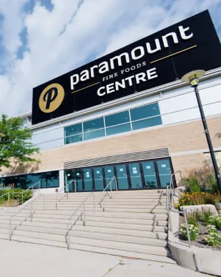 Large escalier extérieur entre des jardins menant à un long édifice comptant neuf portes d'entrée en verre sous une rangée de vastes fenêtres.