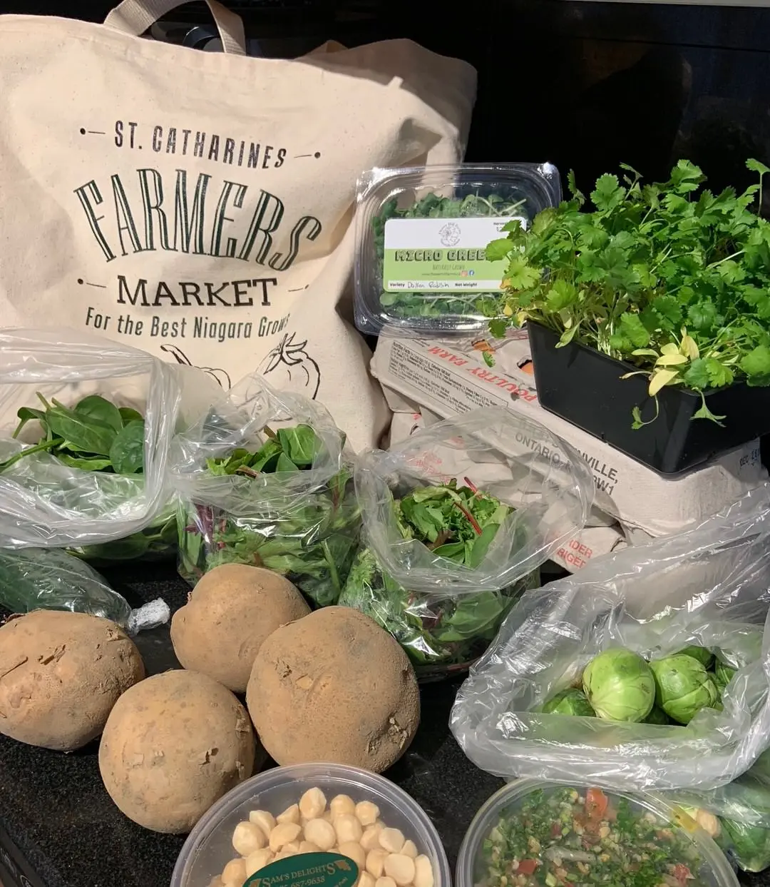 Farmers Market canvas bag on table with 2 cartons of eggs and several potatoes and packages of various green vegetables