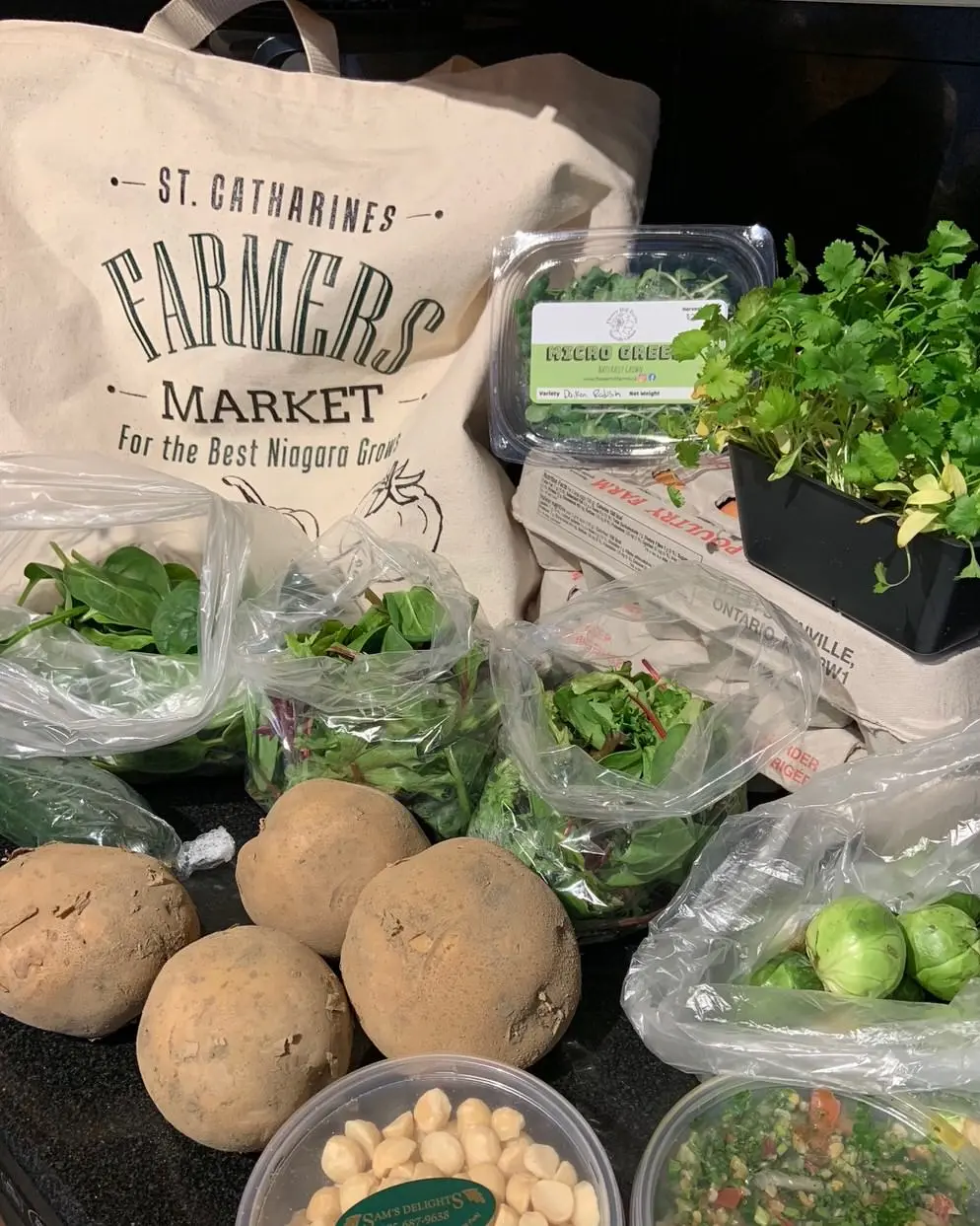 Farmers Market canvas bag on table with 2 cartons of eggs and several potatoes and packages of various green vegetables