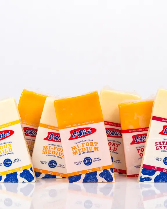 9 labelled packages of alternating orange and yellow cheddar cheese lined up on angles on shiny white reflective tabletop