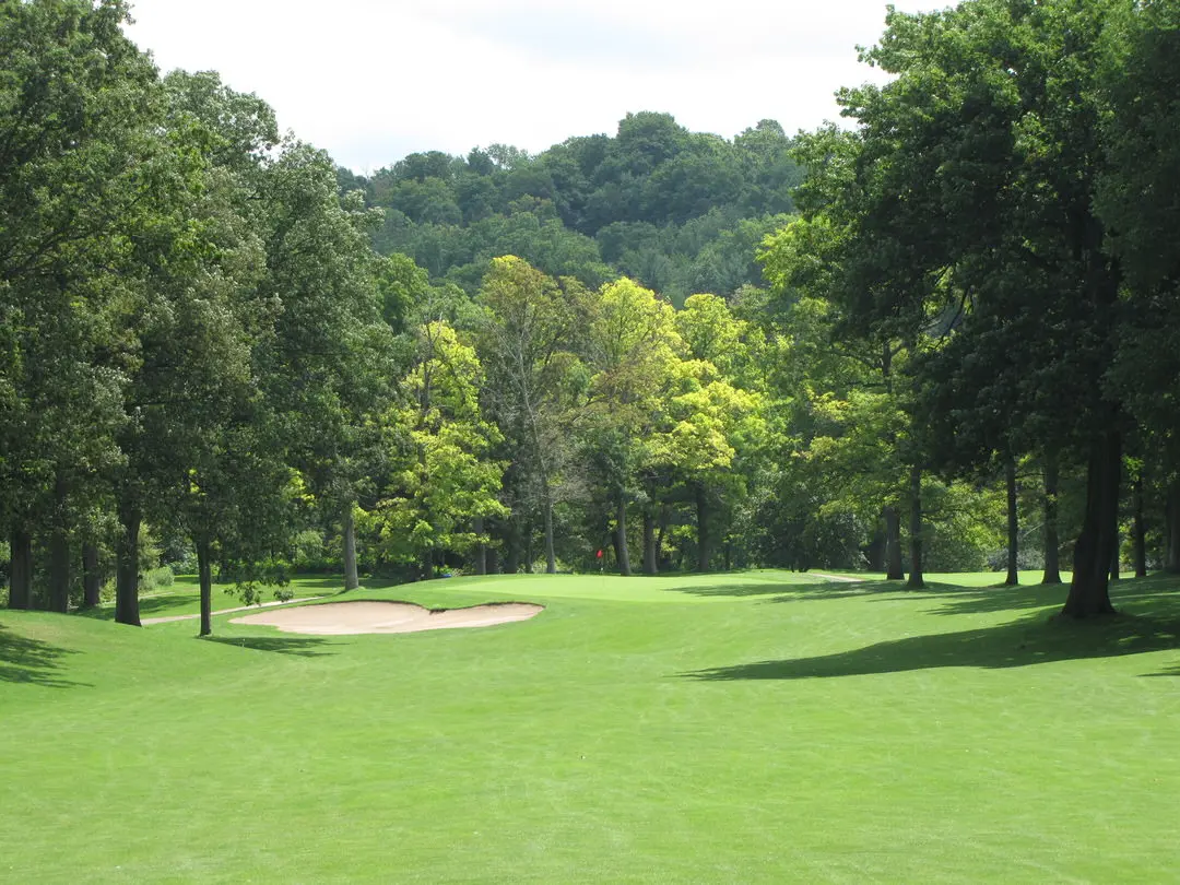 Vaste pelouse verte de terrain de golf avec trappe de sable devant un passage à l'avant-plan et une vaste forêt verte au loin.