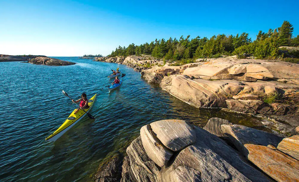 木々が生い茂る岩場に近い湖沿いを漕ぐ3人。