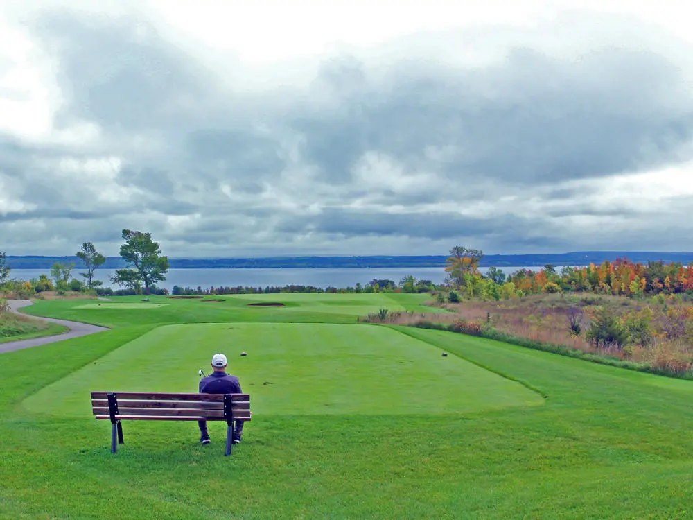 男性がゴルフコースのグリーンを見渡せるベンチに座っている。
