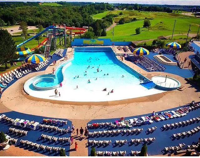 Vogelperspektive auf Menschen, die ein großes Wellenbad genießen, umgeben von Liegestühlen und zwei blauen und gelben Sonnenschirmen