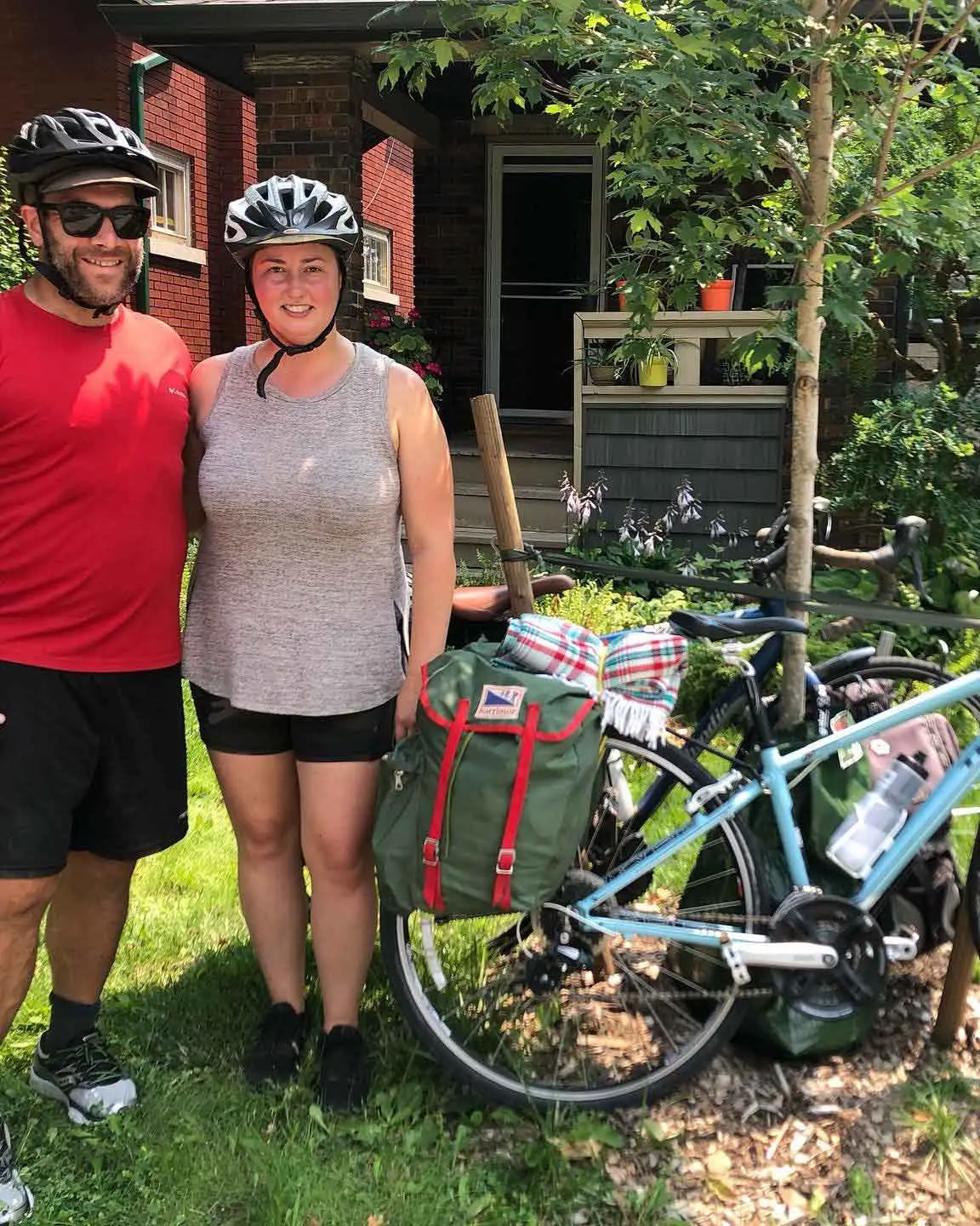 Ein Mann und eine Frau, beide mit Fahrradhelmen, posieren mit einem an einem Baum gelehnten Fahrrad