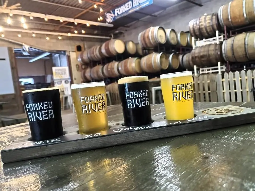 A flight of 4 beers featuring dark and pale ales with barrels in the background