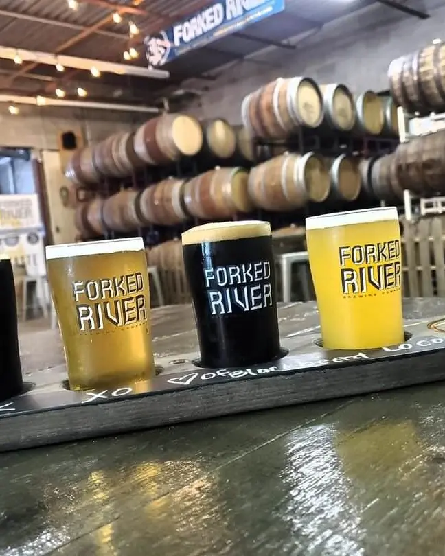 Un vuelo de 4 cervezas con cervezas claras y oscuras con barriles en el fondo.