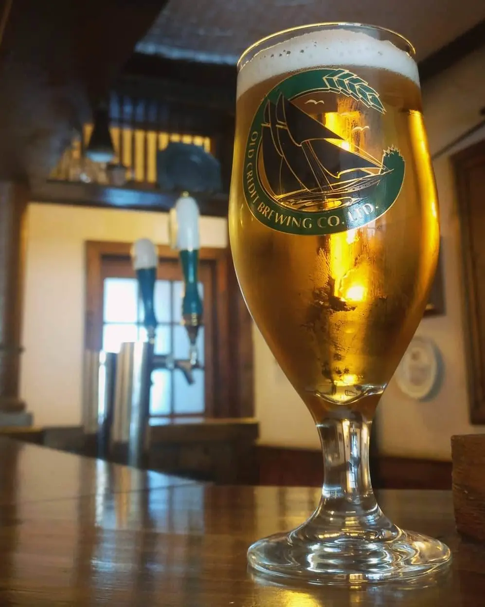 Un primer plano de una cerveza ámbar, con grifos de cerveza en el fondo