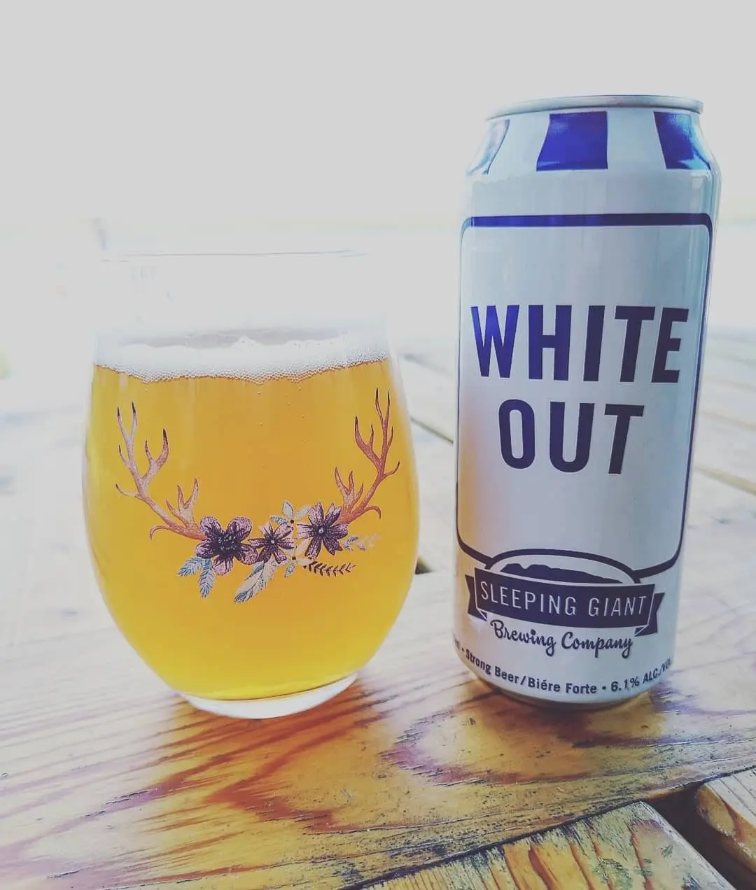 A beautifully adorned glass of beer beside a tall can of beer resting on a table