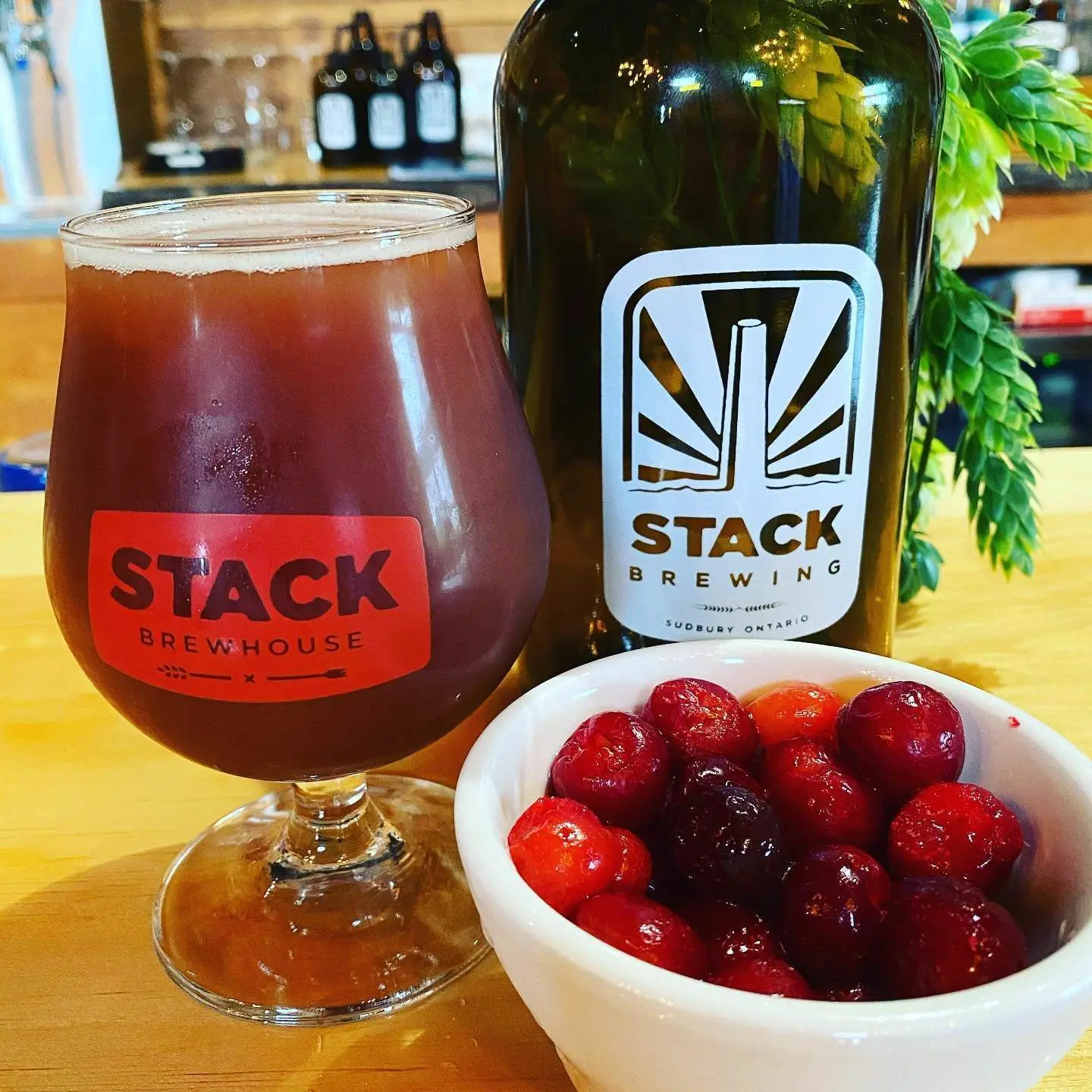 A glass of cranberry beer beside a tall bottle of beer with a small bowl of cranberries