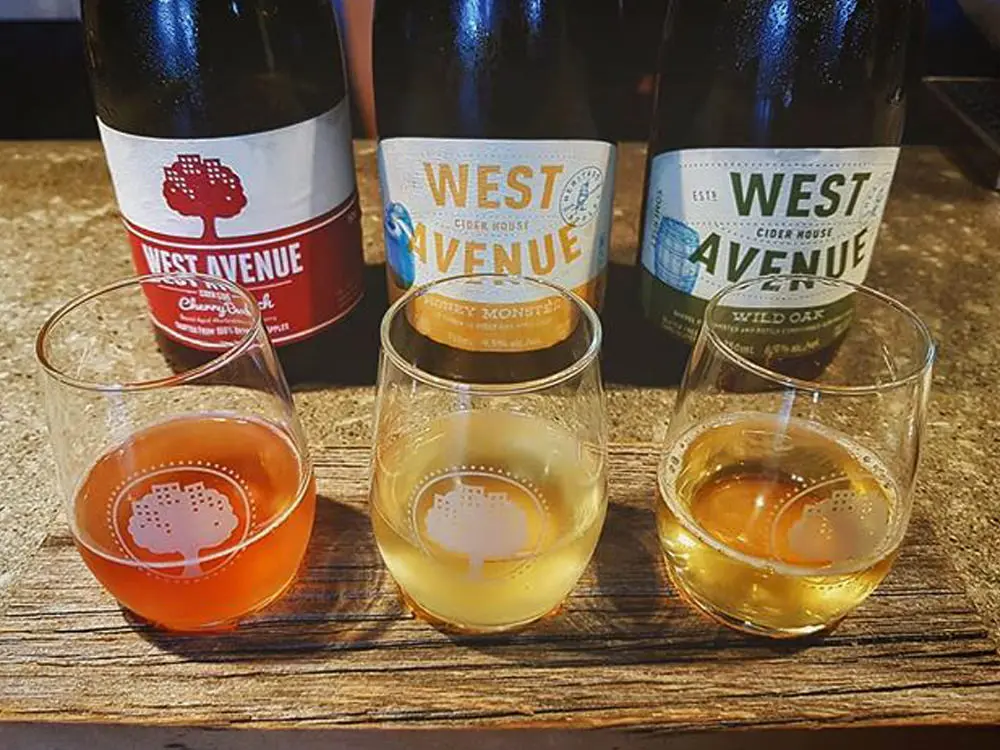 Three bottles of cider lined up behind a tasting flight of three glasses