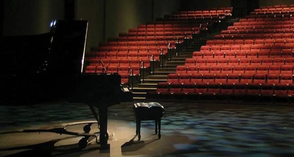 Un piano de cola y un banco de piano en el escenario frente a un auditorio vacío