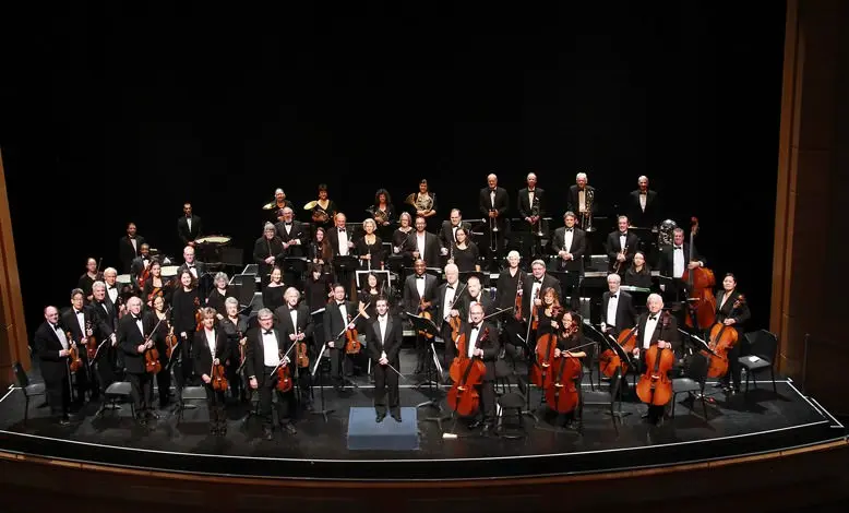 Eine Bühne voller versammelter Musiker umgibt ihren musikalischen Dirigenten