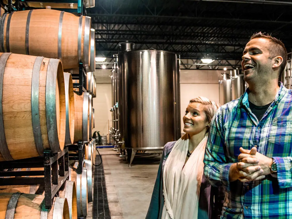 Un couple admire une pile de tonneaux de vin dans une cave viticole