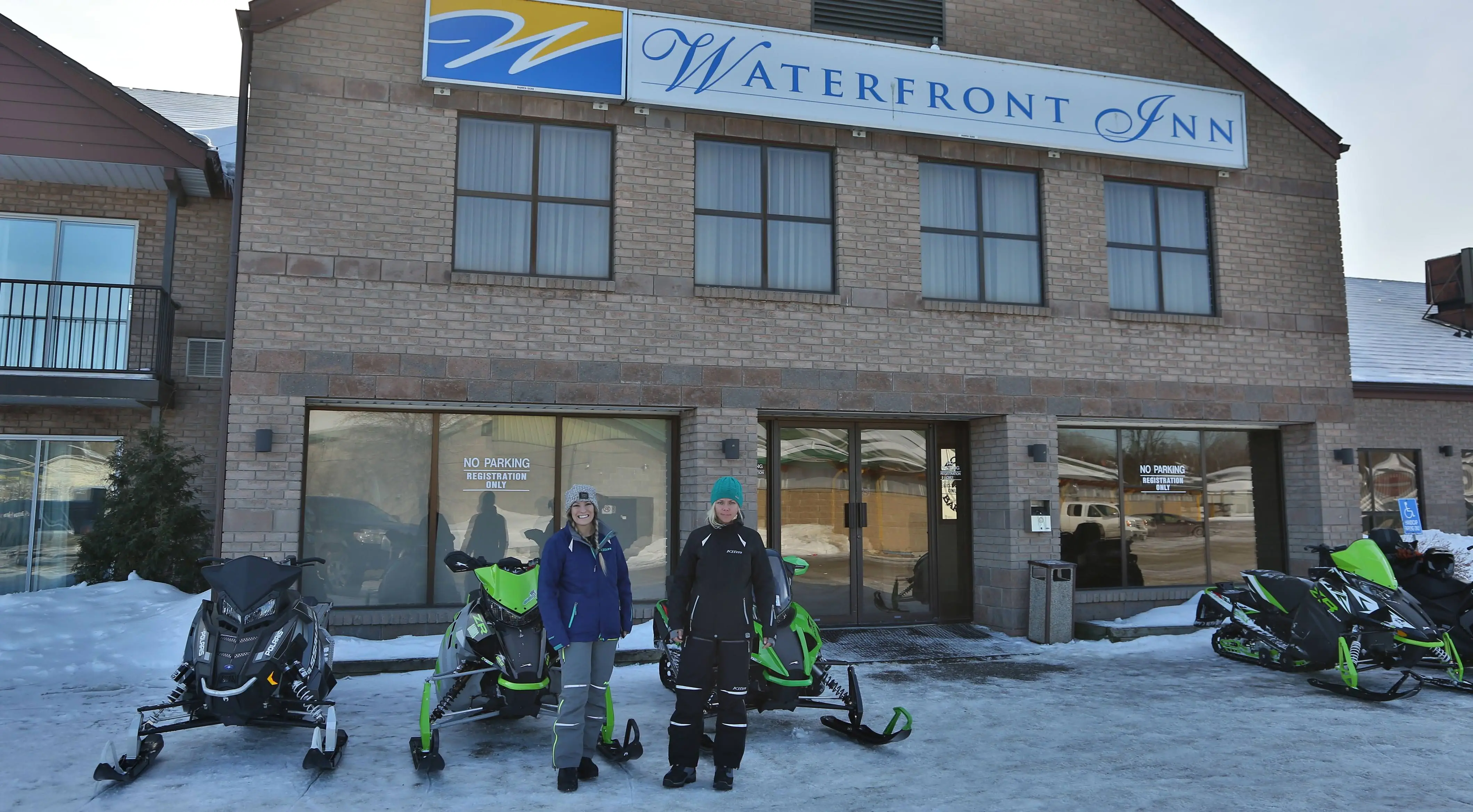 2 Frauen stehen vor Schneemobilen, die vor dem Waterfront Inn . geparkt sind