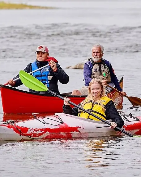 A girl in a kayak in front of two men in a canoe