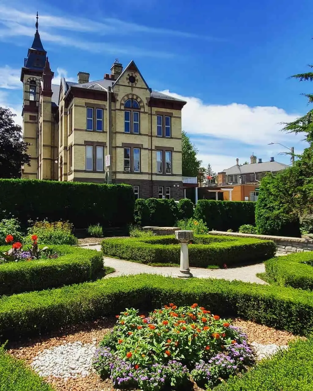 Manicured hedges frame several floral gardens that are located in the front of a large estate home