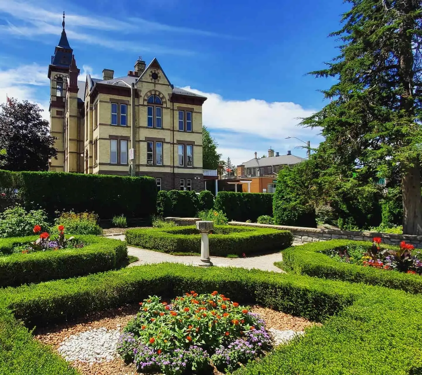 Gepflegte Hecken rahmen mehrere Blumengärten ein, die sich vor einem großen Anwesen befinden