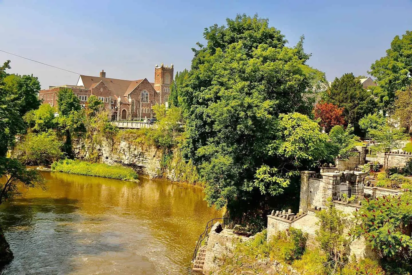  Steinmauern umgeben ein Gewässer und trennen den Garten von der Kirche in der Ferne