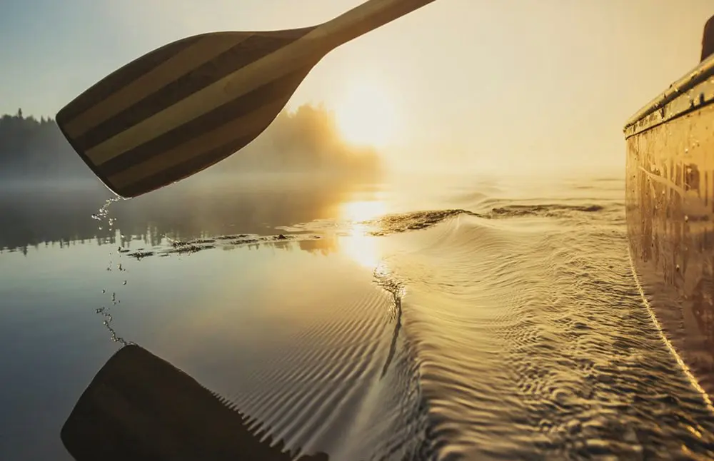 Une pagaie de canoë rame doucement dans l'eau jusqu'au coucher du soleil.