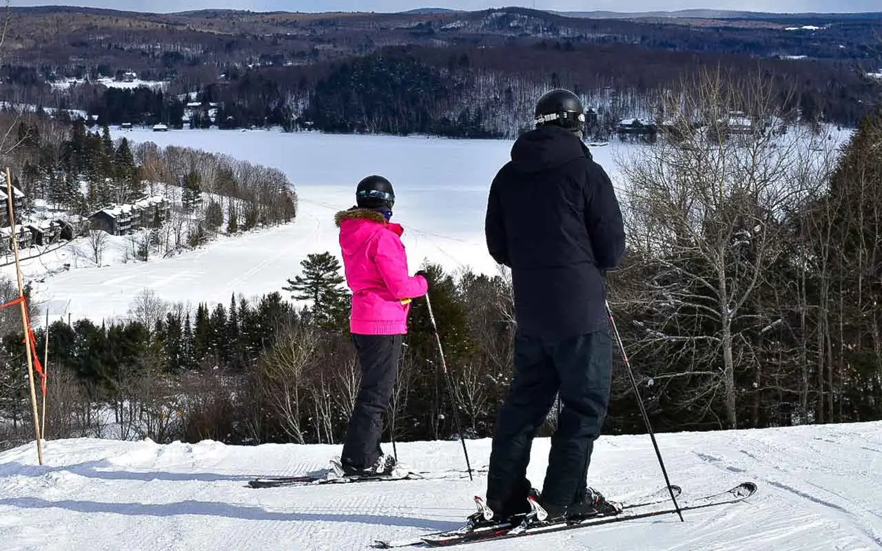 Two people getting ready to ski, while look down at the slopes.