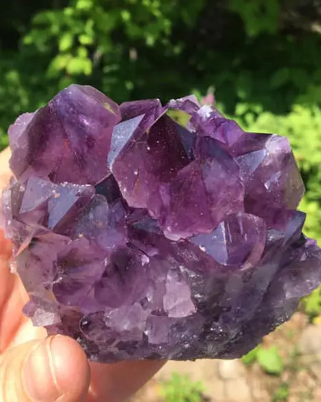 Close-up view of a hand holding an amethyst crystal.