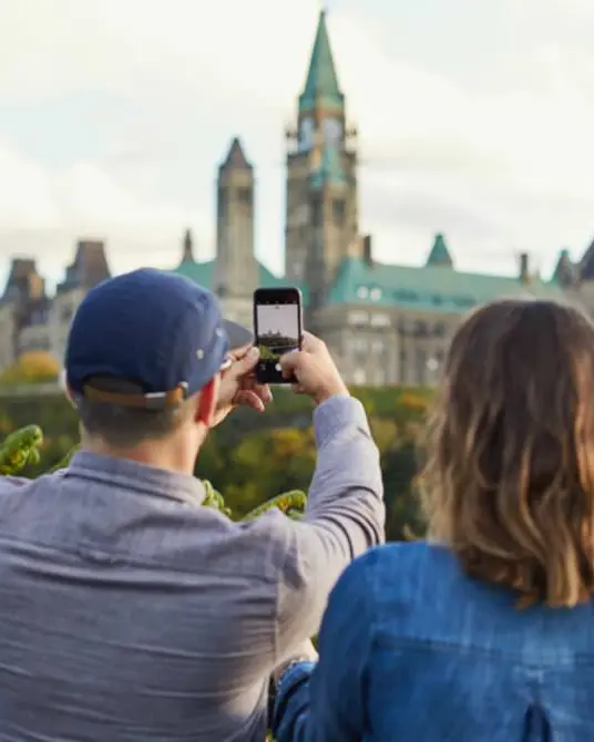 Eine Frau steht neben einem Mann und macht ein Foto vom Parliament Hill in Ottawa.