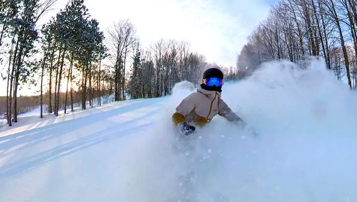 A person snowboarding down a tree-lined hill.