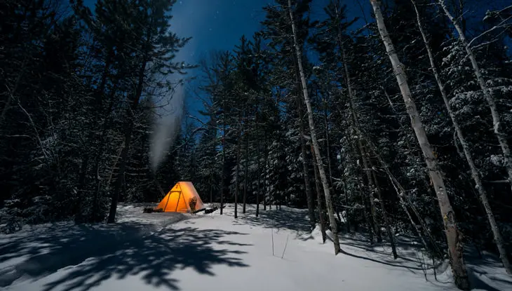 Una tienda de campaña se ilumina en la oscuridad durante un viaje de campamento invernal en el bosque.