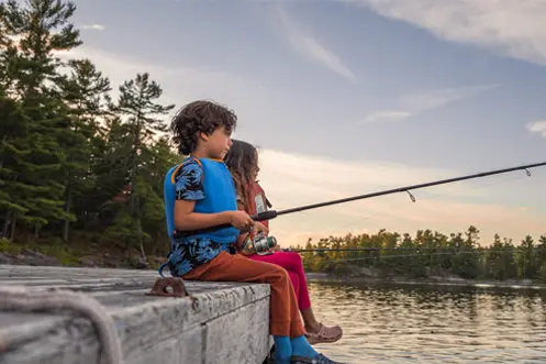 A boy and a girl fishing while sitting on a dock.