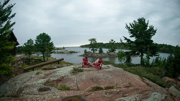 Deux femmes assises sur un rocher, dans des chaises muskoka rouges, regardant au-dessus de l'eau
