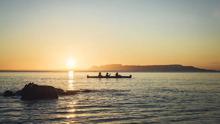 Three people paddling in a canoe during sunset with the Sleeping Giant in the background