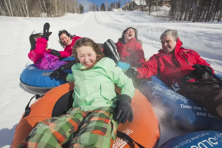 A group of people laughing while tubing down a snowy hill