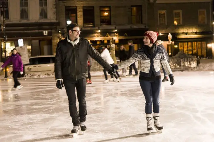 Two people holding hands and smiling at each other while ice skating at night.