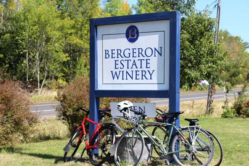 Several bicycle are parked below a large sign to a winery.
