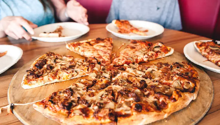 Se corta una pizza grande, de tamaño familiar, sobre una tabla de madera redonda para compartir.