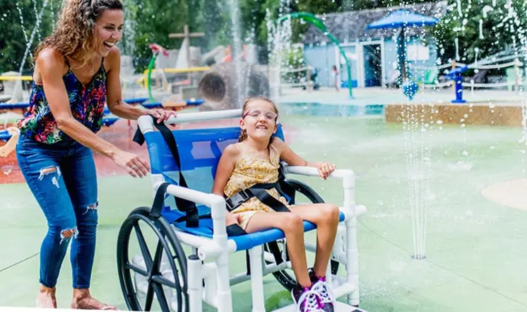 Une femme et une jeune fille assise dans un fauteuil roulant aiment jouer dans une fontaine d’eau.