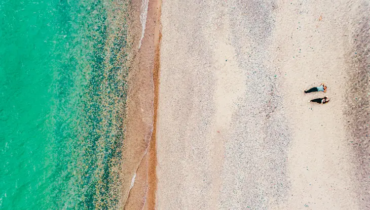 Vista aérea de dos personas tumbadas en la orilla de una playa de arena blanca del lago Huron.