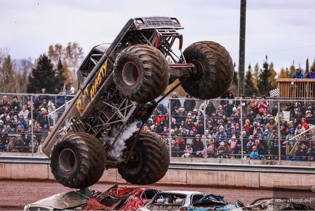 観客が見守る中、モンスタートラックが押しつぶされた車の列の上空に浮かんでいる。