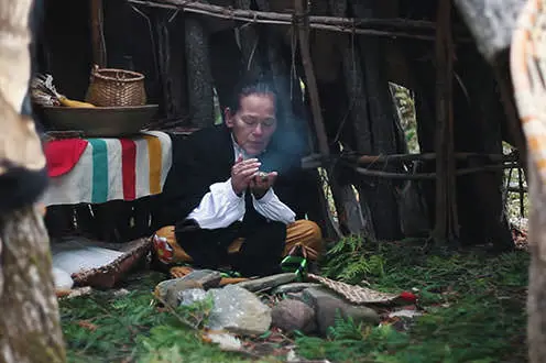 A woman in traditional clothing tends to the fire in a recreated Indigenous dwelling at Lang Pioneer Village