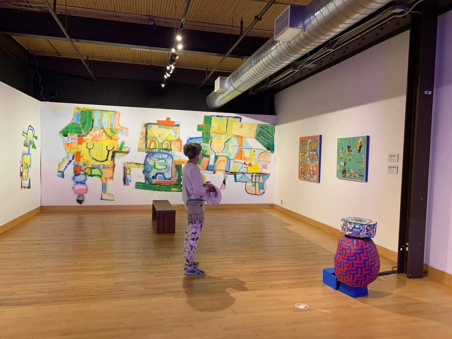 A woman wearing a mask is admiring the art in a room.