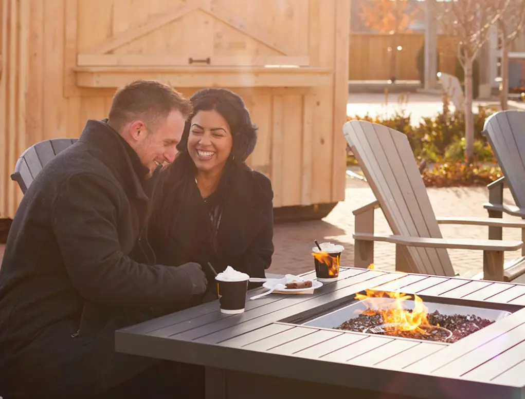 Ein Paar macht es sich neben einer Feuerstelle im Freien gemütlich und genießt heiße Schokolade.