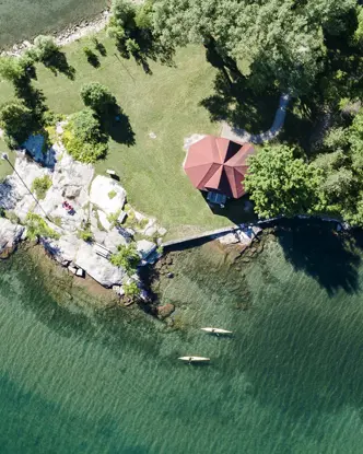 세인트 로렌스 강의 1000개 섬 지역에서 바위가 많은 해안선, 깨끗한 물, 그리고 카약을 타는 두 명의 사람을 촬영한 공중 사진입니다.