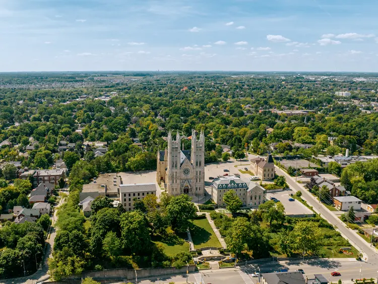Luftaufnahme der Innenstadt von Guelph mit der Basilika Unserer Lieben Frau Immaculata mit ihren zwei Türmen, umgeben von baumgesäumten Straßen und der Stadtlandschaft.